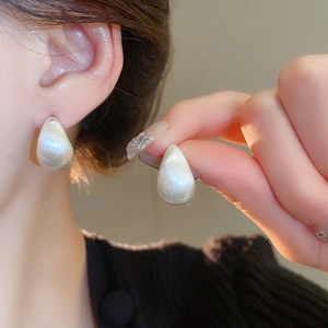 Close-up of minimalist gold-plated teardrop stud earrings with brushed pearl finish