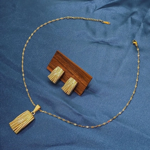 Detailed view of textured gold rectangle necklace and earrings set on blue silk