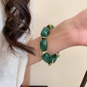 Detailed close-up of chunky green resin beads with gold glitter on a stylish metal bracelet