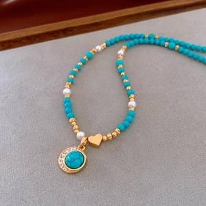 Macro shot of turquoise pendant with rhinestones and gold heart on 18K plated necklace
