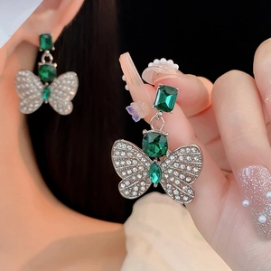 Gros plan d'une boucle d'oreille papillon argentée avec pierres vertes et cristaux