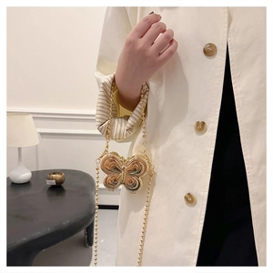 Detailed view of a mini golden butterfly-shaped metal chain bag worn on a beige trench coat