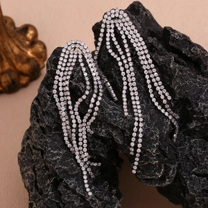 Detail of silver tassel earrings with micro-set zircons on a textured stone backdrop