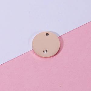 Polished rose gold round stainless steel pendant with small crystal on a pink background