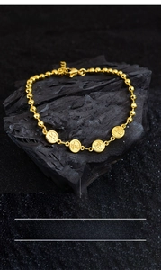 Close-up of gold beaded bracelet with round charms engraved with Ping An symbols on charcoal