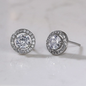 Macro detail of silver floral zircon stud earrings on light marble surface