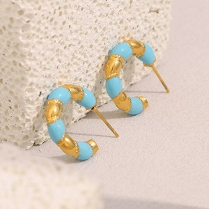Close-up of C-shaped hoop earrings with gold plating and light blue enamel on stone
