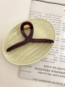 Macro detail of dark red 13cm hair claw clip on ceramic dish with vintage paper