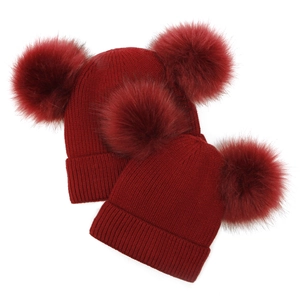 Detail view of dark red knitted beanie set with faux fur double pom poms for mother and baby