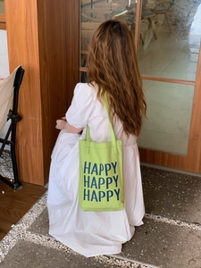 Detail view of light green canvas tote bag with Happy print on a white dress model