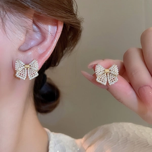 Macro shot of bow earrings with delicate faux pearls and crystals on a golden base