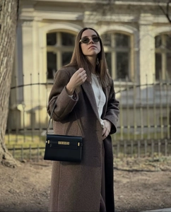 Close-up of black leather handbag with gold buckle styled with a brown wool coat