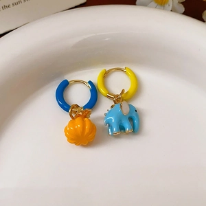 Macro detail of asymmetric enamel pumpkin and elephant charms on hoop earrings