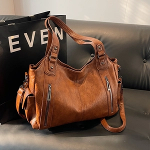Vintage brown leather tote bag with rivets and dual handles on a sofa background