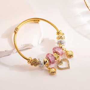 Close-up of golden beaded bracelet with pink glass beads and heart charms on white rock