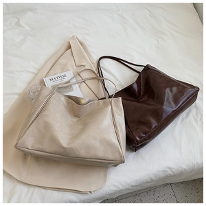 Detail view of large faux leather tote bags in beige and coffee colors on white bedding