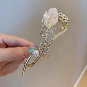 Close-up of golden feather hair clip with sparkling rhinestones and pearl details