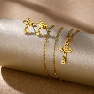Detailed view of golden cross pendant and stud earrings set on elegant metallic texture