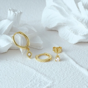Macro shot of gold hoop earrings with diamond charms and studs on a white pedestal