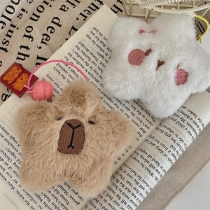 Detail of plush star keychains with capybara and bear embroidery on book background
