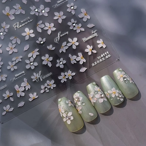 Macro shot of 3D embossed white flower nail stickers with crystal accents on green base