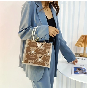 Detail of a brown bear canvas tote bag held by a model in a blue suit indoors
