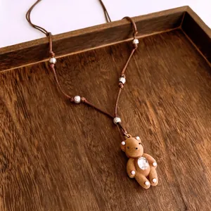 Brown flocked bear pendant necklace with teardrop gem and beaded cord on wood tray
