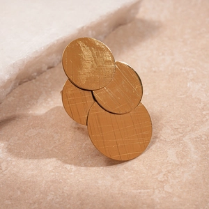 Brushed golden geometric stacked circular metal ring on a warm mineral stone background