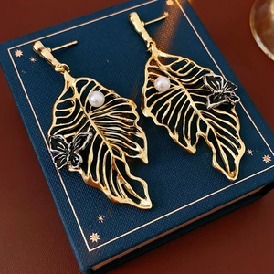 Close-up of golden hollow leaf earrings with pearls and black butterflies on a jewelry box
