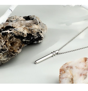 Detailed close-up of a silver minimalist cylindrical pendant necklace on natural stone