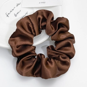 Macro detail of a dark brown satin scrunchie with a glossy silk texture on a white plate