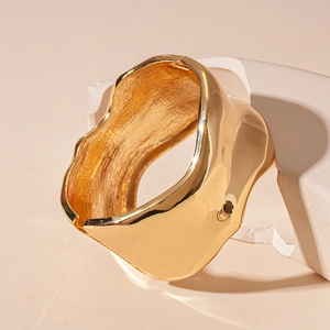 Macro view of wide gold irregular metal cuff with liquid-like texture on stone base