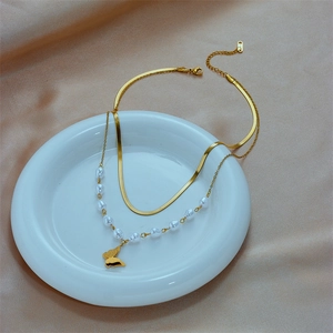 Double-layered gold necklace featuring white pearls and butterfly pendant on ceramic tray