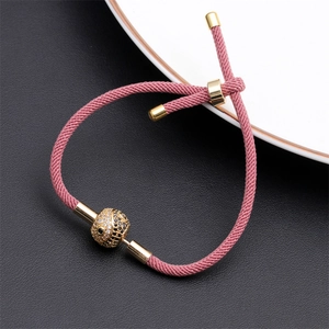 Close-up of pink braided rope bracelet with gold slider and pavé crystal ball charm
