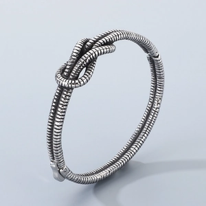 Detailed close-up of a silver knot-shaped metal bracelet with intricate textured thread details