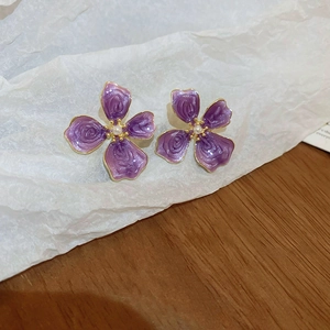 Macro detail of purple petal floral earrings with white pearl center and gold-tone edges