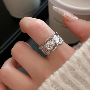 Makroaufnahme eines silbernen, hohlen Rosenrings mit floralem Relief am Finger