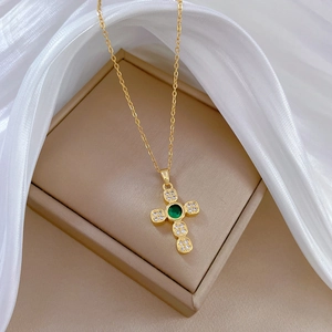 Detail of gold cross pendant with green gemstone and small diamonds on a jewelry box