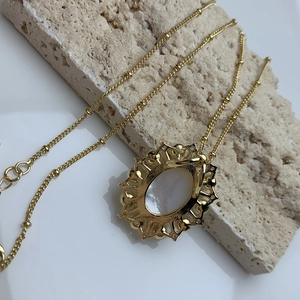 Vintage golden necklace with white shell pendant on natural stone surface background