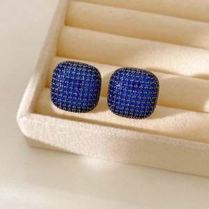 Macro shot of square dark metal stud earrings paved with deep blue cubic zirconia stones