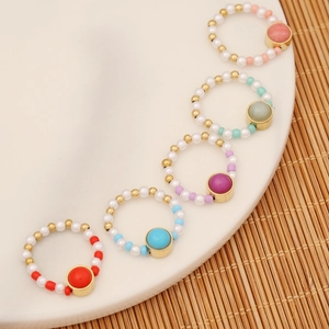 Five colorful handmade beaded rings with natural stones and gold beads on white plate