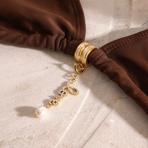 Macro view of crystal 'Love' charm with artificial pearl on brown bikini fabric
