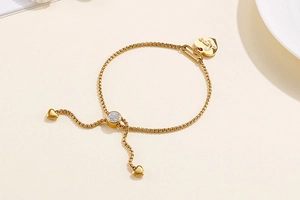 Adjustable golden heart bracelet featuring a zircon-studded slide clasp and dual mini charms
