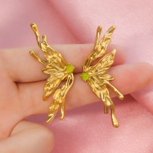 Artistic golden butterfly earrings with green natural stones shown on pink velvet