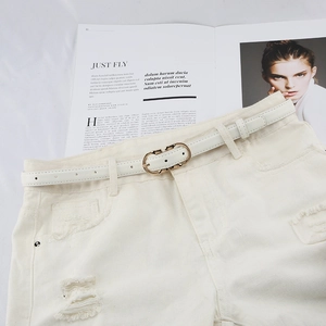 Detailed view of white slim leather belt with gold oval buckle on denim shorts