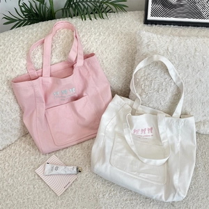 Close-up of bow embroidery and slogan details on canvas tote bags in pink and white