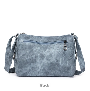 Detail view of the back zipper pocket on a blue-grey washed denim texture crossbody bag
