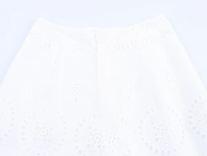 Close-up of white wide-leg trousers showing hollow embroidery and button waist detail