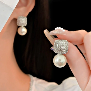 Detailed close-up of a model wearing square zircon stud earrings with white pearls