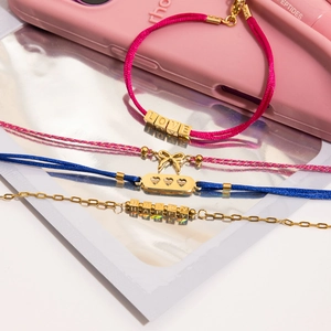 Détail de bracelets tissés avec pendentifs LOVE et HAPPY dorés sur fond rose brillant